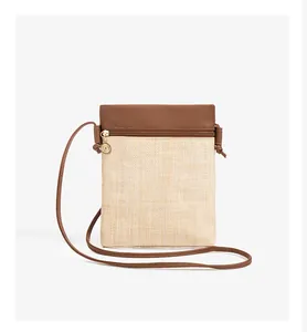 Close-up of straw woven phone bag featuring brown leather flap and gold zipper charm