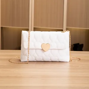Close-up of white heart quilted bag featuring a large gold heart lock and chain strap