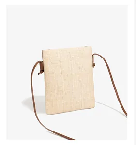 Detail of hand-woven straw phone bag with natural texture and brown crossbody strap