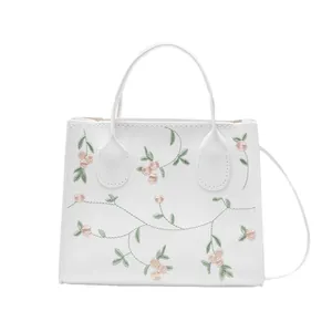 White mini handbag with floral embroidery, featuring dual handles and a long shoulder strap