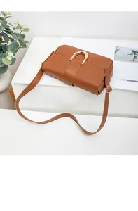 Macro view of caramel brown shoulder bag featuring a golden horseshoe metal buckle detail