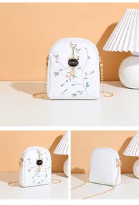 Detail of white chain bag featuring floral embroidery and a golden cat head pendant