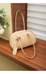 Detailansicht beige Handtasche mit Litschimuster-Textur und Logo-Anhänger