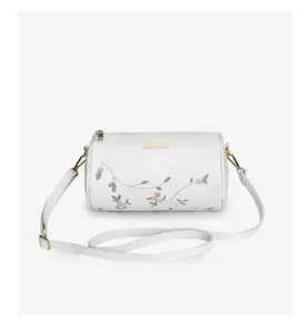 Détail de broderie florale sur un sac cylindrique blanc avec des finitions dorées