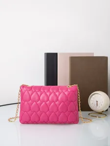 Detail of rose pink crossbody bag with heart-quilted texture and gold chain strap