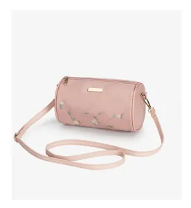 Détail d'un sac cylindrique rose avec broderie florale et finitions métalliques dorées