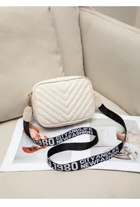 Detail of cream white crossbody bag with V-quilted texture and lettered fabric strap