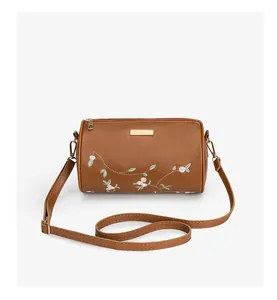 Détail de broderie florale sur un sac bandoulière cylindrique en cuir PU marron