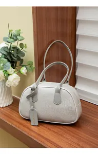 Detail der hellgrauen Handtasche mit Leder-Litschi-Struktur und stilvollem Anhänger