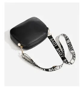 Detail of black crossbody bag with wide strap featuring LOVE lettering and gold hardware