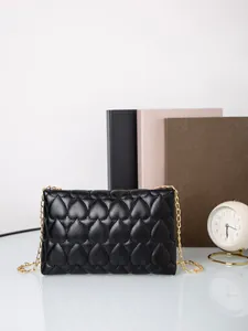 Detail of black quilted shoulder bag with heart pattern and gold chain strap