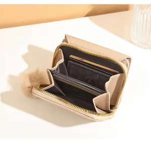 Detail view of beige multi-slot accordion card holder wallet with plush ball charm