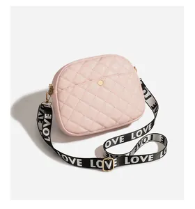 Detail of pink quilted crossbody bag featuring a metal button and LOVE printed strap