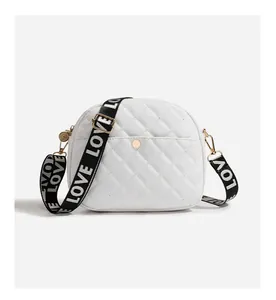Detail of white quilted camera bag with gold hardware and LOVE patterned shoulder strap