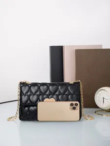 Detail of black heart-quilted crossbody bag with gold chain and smartphone for size scale