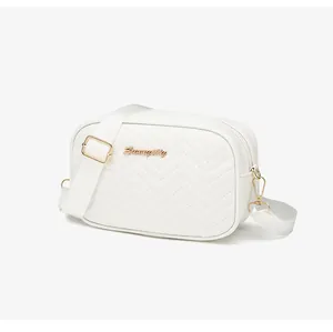 Detail of white quilted crossbody bag with golden V-stitching and adjustable fabric strap