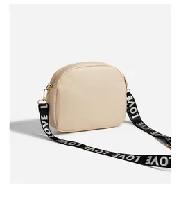 Detail of cream crossbody camera bag with embroidered quilted pattern and LOVE strap