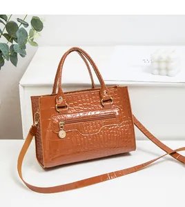 Detail der braunen Handtasche mit Krokodilprägung und Goldreißverschlüssen auf Weiß