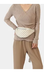 Detail of a beige monogram crossbody bag with letter print shown on a model