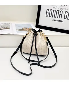 Détail du sac seau en paille tressée avec cordon noir et accent de chaîne dorée