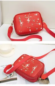 Close-up of red crossbody camera bag featuring floral embroidery and wide fabric strap
