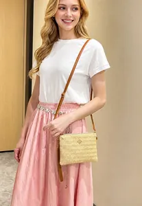 Gros plan du sac bandoulière en paille beige avec texture tissée et lanière marron