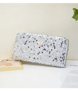 Dettaglio di paillettes argento e decoro a farfalla su pochette lunga con cerniera