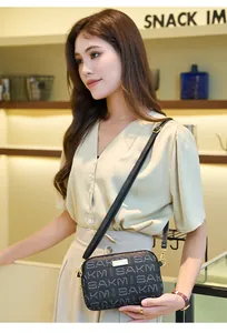 Detail view of black crossbody camera bag with SAKM letter print and gold hardware