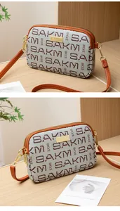 Detail of dual zipper closure and letter print on textured leather crossbody bag