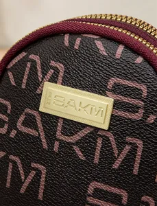 Detail of SAKM monogram pattern on brown leather bag with gold metal plate and red trim