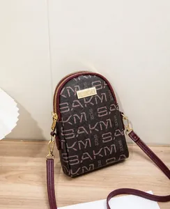 Detail view of the SAKM crossbody bag with double zipper and gold metal logo plaque