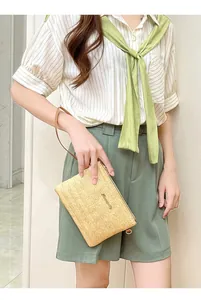 Dettaglio della pochette in paglia intrecciata con cinturino in pelle marrone