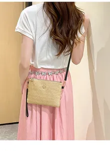 Détail d'un sac à bandoulière en paille tressée avec logo fleur sur un mannequin lifestyle