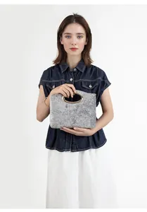 Close-up of grey textured fabric handbag featuring a round gold metal handle on model