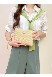 Dettaglio di una pochette in paglia intrecciata beige con logo dorato e cinturino in pelle