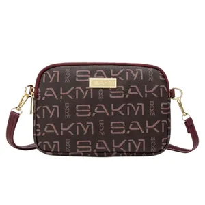 Burgundy crossbody bag with SAKM logo print and gold hardware on white background