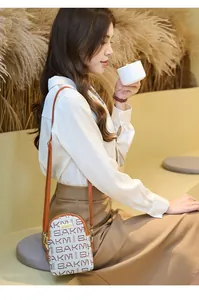 Close-up of small white crossbody bag with red SAKMY letter print and brown strap