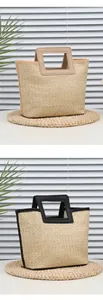 Detailed view of woven straw handbags with black and beige leather trim handles