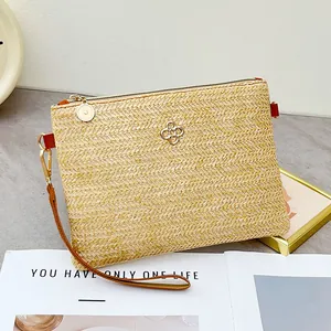 Pochette en paille tissée main avec logo fleur doré et dragonne marron sur une table