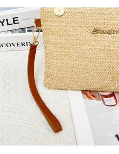 Dettaglio pochette in paglia intrecciata con logo dorato, chiusura magnetica e cinturino