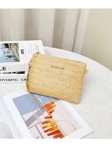 Dettaglio di pochette in paglia beige con trama a spina di pesce e logo metallico