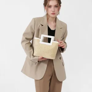 Minimalist woven straw handbag with contrast white leather handles shown on a model