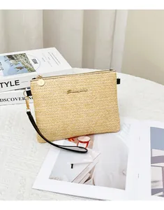 Dettaglio di pochette in paglia intrecciata con trama a V e placca logo dorata