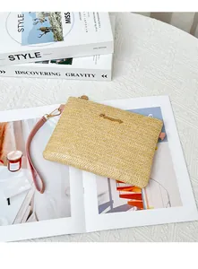 Dettaglio della pochette in paglia intrecciata con cinturino rosa e logo dorato su riviste