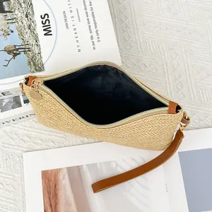 Pochette in paglia con cerniera dorata e cinturino in pelle marrone su sfondo elegante