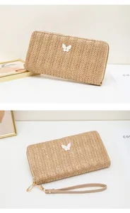 Detalle de billetera larga de paja tejida con dije de mariposa y correa de muñeca