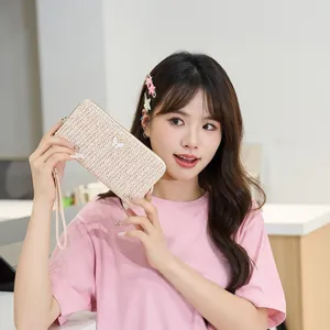 Cartera larga de paja en blanco crema con colgante de mariposa y correa de muñeca