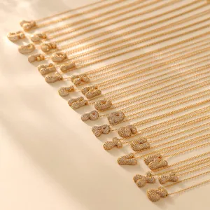 Close-up of golden bubble letter necklaces with sparkling zircon pave on beige background