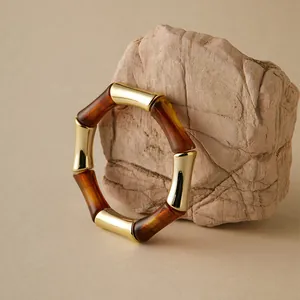 Dettaglio del bracciale in acrilico ambra e oro su un supporto in pietra testurizzata