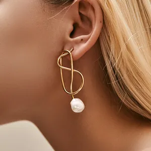Nahaufnahme eleganter goldener Tropfenohrringe mit Barockperlen an einem Modell